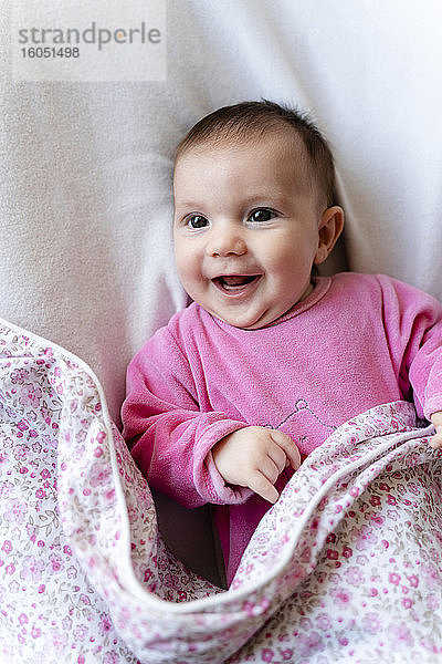Porträt eines glücklichen kleinen Mädchens im rosa Pyjama auf dem Bett liegend
