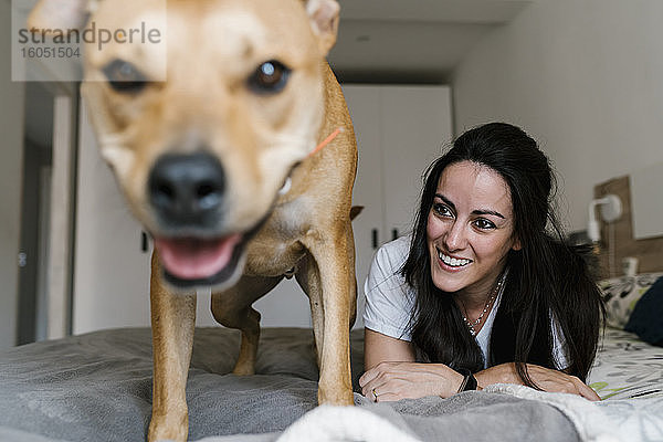 Lächelnde Frau sieht ihren Hund an  während sie zu Hause auf dem Bett liegt