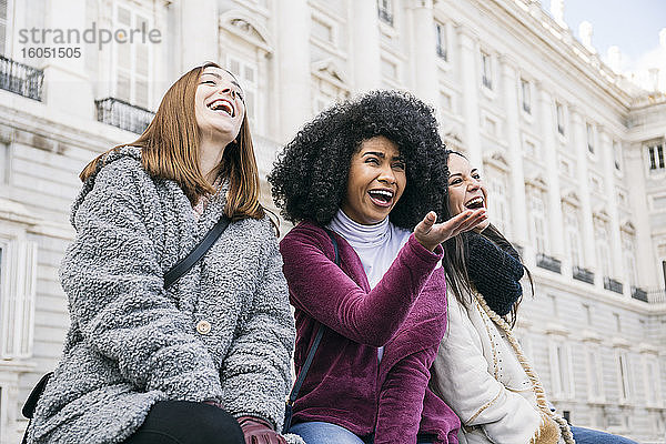 Multiethnische Freundinnen  die lachend vor dem Königspalast in Madrid sitzen  Spanien