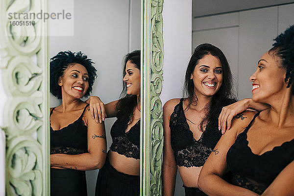 Glückliche Freundinnen in schwarzer Kleidung stehen vor einem Spiegel zu Hause