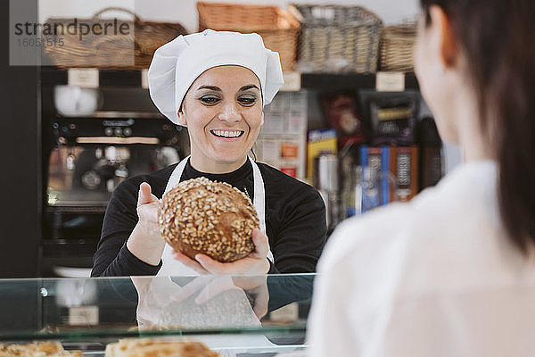 Glückliche Bäckerin  die einem Kunden in einer Bäckerei Vollkornbrötchen verkauft