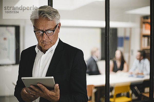 Älterer Geschäftsmann mit digitalem Tablet  Mitarbeiter arbeiten im Hintergrund