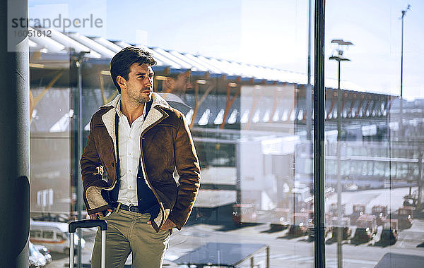 Nachdenklicher Geschäftsmann steht mit den Händen in den Taschen am Fenster im Abflugbereich eines Flughafens