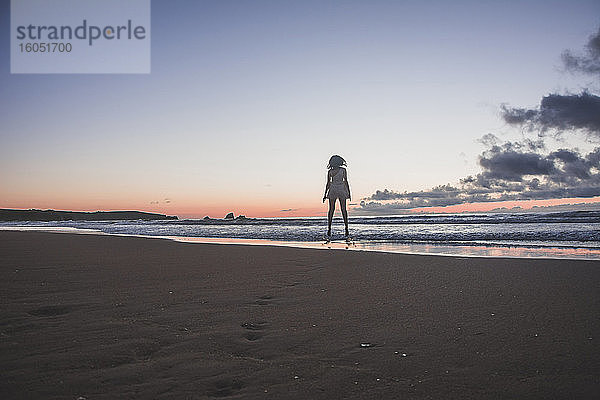 Silhouette junge Frau steht am Strand gegen den Himmel bei Sonnenuntergang