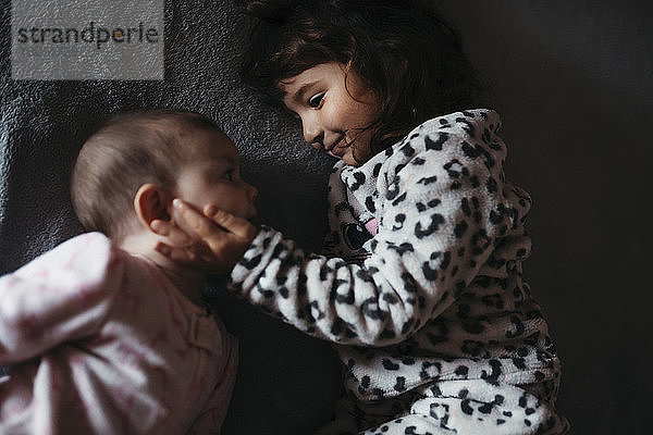 Mädchen berührt die Wangen ihrer kleinen Schwester  während sie auf dem Bett liegt