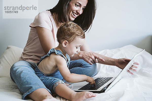 Mutter und kleines Mädchen benutzen Laptop auf dem Bett zu Hause