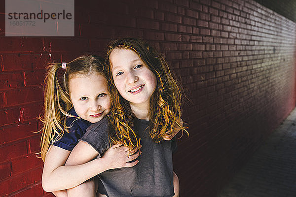 Nettes Mädchen umarmt Schwester  während sie gegen eine Mauer steht