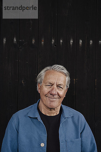 Porträt eines selbstbewussten älteren Mannes  der an einer Holzwand steht