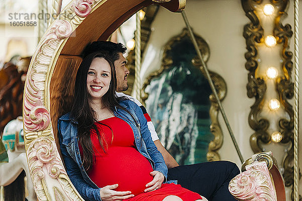 Glückliche schwangere Frau sitzt mit einem Mann auf einem Karussell in einem Vergnügungspark  Cascais  Portugal