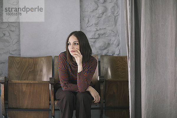 Nachdenkliche junge Frau sitzt auf einem Stuhl in einem Atelier für Bekleidungsdesign