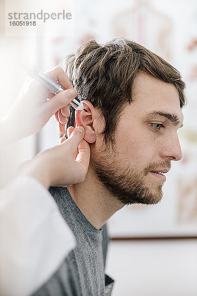 Heilpraktikerin gibt Mann Akupunktur mit Akupen im Ohr