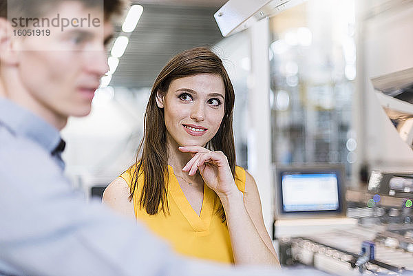 Lächelnde Geschäftsfrau sieht einen männlichen Mitarbeiter in einer Fabrik an