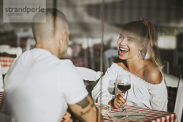 Glückliche Frau  die ein Weinglas hält und ihren Freund in einem Restaurant durch ein Fenster betrachtet