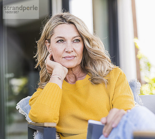 Porträt einer nachdenklichen reifen Frau  die mit einem digitalen Tablet auf einer Terrasse sitzt und in die Ferne schaut