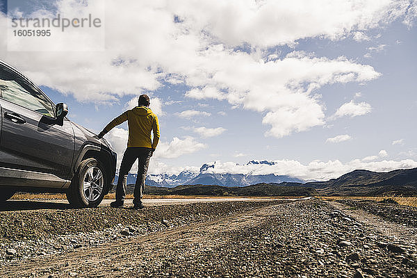 Älterer Mann steht neben einem Auto auf einer unbefestigten Straße im Torres Del Paine National Park  Patagonien  Chile