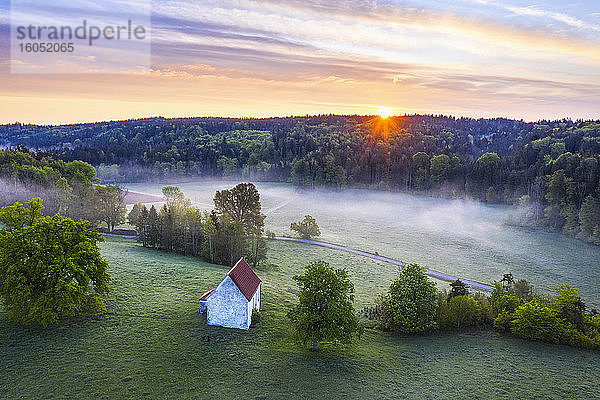 Deutschland  Bayern  Egling  Drohnenansicht der Kapelle Saint Koloman bei nebligem Frühlings-Sonnenaufgang