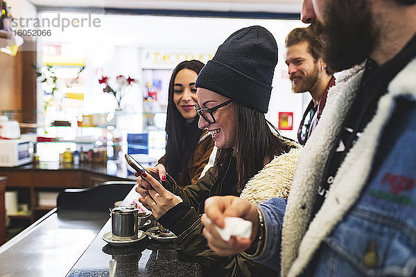 Lächelnde Frau  die ein Smartphone benutzt  während sie sich mit Freunden in einem Café amüsiert