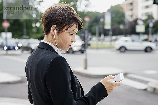 Nahaufnahme eines weiblichen Berufstätigen  der ein Smartphone benutzt  während er auf einer Straße in der Stadt steht