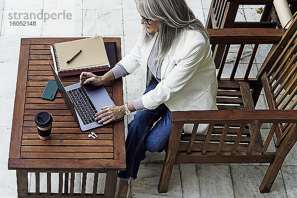 Eine Unternehmerin benutzt einen Laptop und sitzt an einem Holztisch im Garten