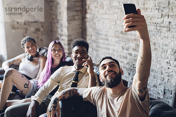 Gruppe von Freunden sitzt auf dem Sofa in einem Loft und macht ein Selfie