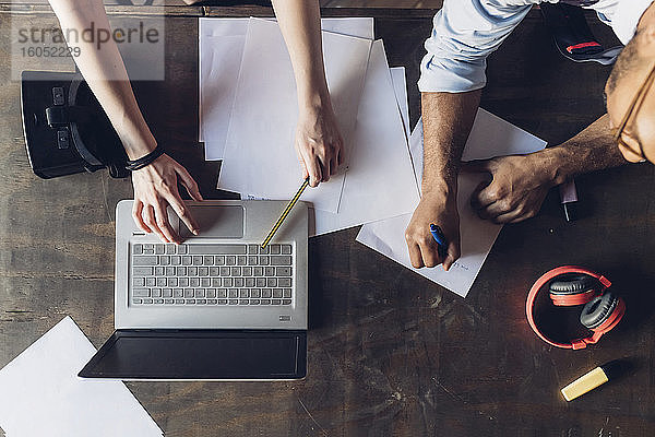 Zwei kreative Geschäftsleute arbeiten mit Laptop und Papieren auf einem Holztisch