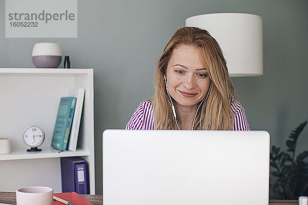 Lächelnde Geschäftsfrau mit Kopfhörern und Laptop im Büro