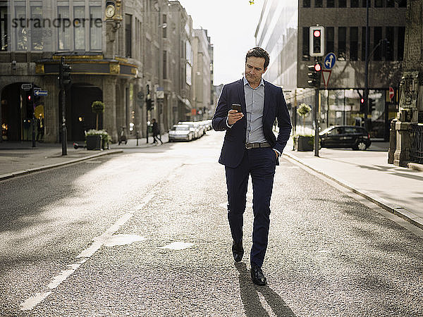 Älterer Geschäftsmann  der auf einer Straße in der Stadt spazieren geht und ein Smartphone benutzt