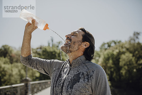 Nahaufnahme eines reifen Mannes  der Wasser trinkt  während er in einem Park vor einem klaren Himmel steht