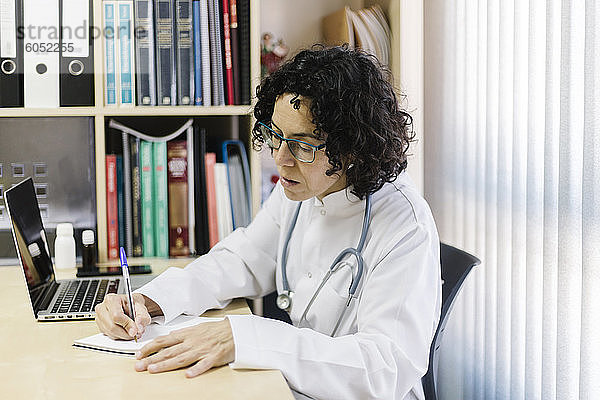 Ärztin schreibt am Laptop  während sie am Schreibtisch im Büro sitzt