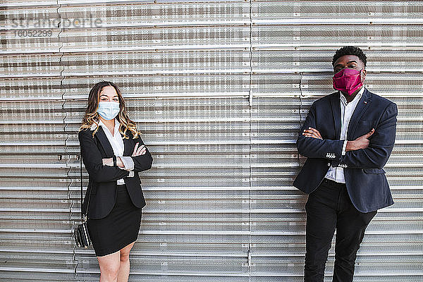 Geschäftsleute mit Masken und verschränkten Armen stehen an einer Wand in der Stadt