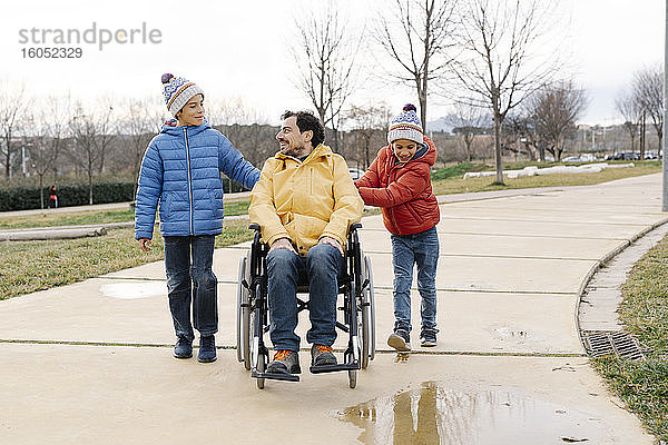 Söhne unterhalten sich und helfen ihrem im Rollstuhl sitzenden Vater im Park