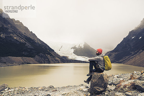 Älterer Mann mit Rucksack sitzt auf einem Felsen am See in Patagonien  Argentinien