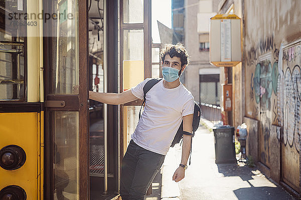Junger Mann mit Maske hängt am Eingang einer Straßenbahn
