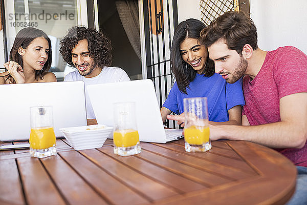 Fröhliche junge Freunde teilen sich Laptops im Hinterhof