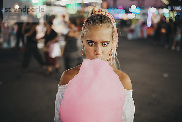 Nahaufnahme einer Frau  die ein Gesicht macht  während sie in einem Vergnügungspark Zuckerwatte isst