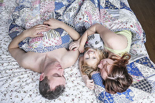 Glückliches Mädchen mit Eltern zu Hause im Bett liegend