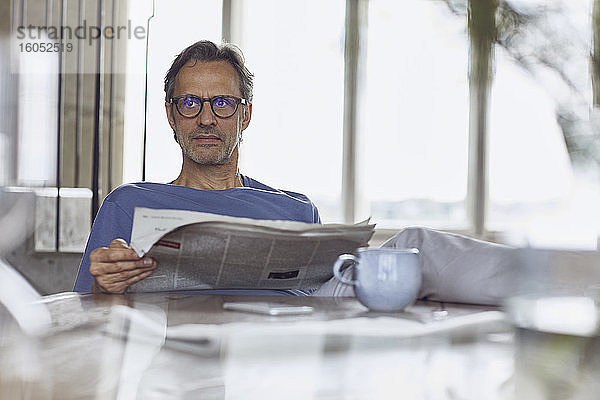 Älterer Mann sitzt am Tisch in einer Dachgeschosswohnung und liest Zeitung