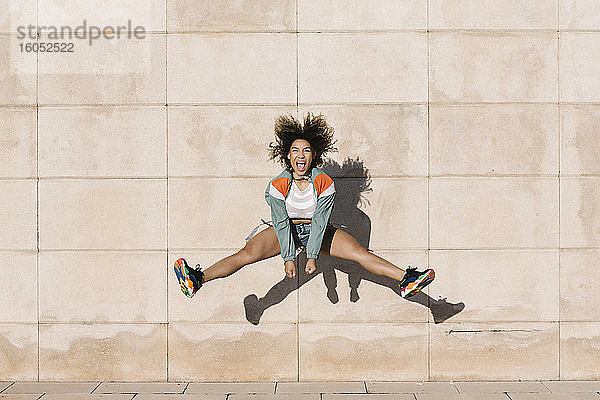 Aufgeregte junge Frau  die schreit  während sie an einem sonnigen Tag gegen die Wand springt