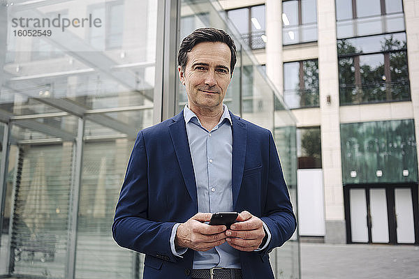 Porträt eines selbstbewussten reifen Geschäftsmannes mit Smartphone in der Stadt