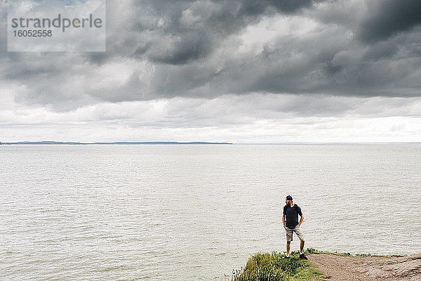 Mann steht auf einer Klippe und blickt auf das Meer vor Gewitterwolken