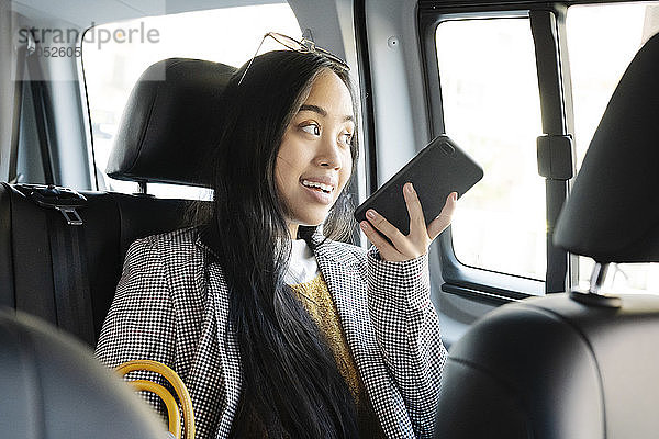 Frau  die im Taxi sitzend über ihr Smartphone spricht