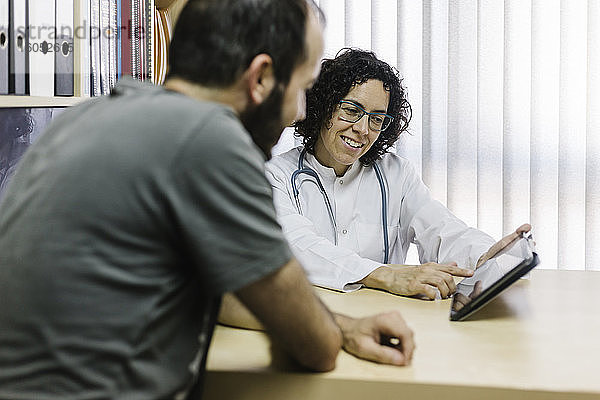 Eine lächelnde Ärztin zeigt einem Patienten in einer Klinik ein digitales Tablet
