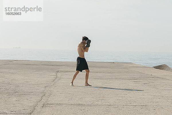Männlicher Athlet ohne Hemd  der am Hafen stehend an einem sonnigen Tag Boxen übt