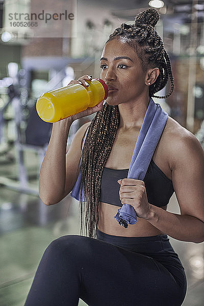 Selbstbewusste Sportlerin mit geflochtenem Haar  die im Fitnessstudio stehend Wasser trinkt