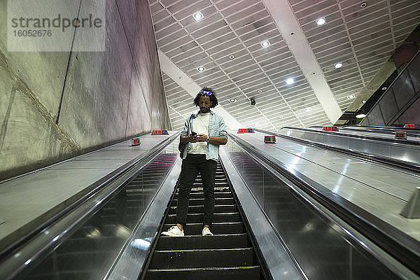 Junger trendiger Mann benutzt Smartphone auf Rolltreppe in U-Bahn-Station