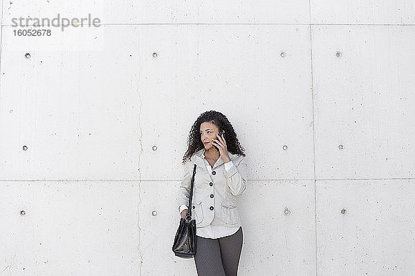 Stilvolle Geschäftsfrau im Gespräch über ein Smartphone  während sie an der Wand steht