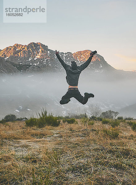 Junger männlicher Tourist mit ausgestreckten Armen  der bei Sonnenaufgang auf einen Berg springt  Leon  Spanien