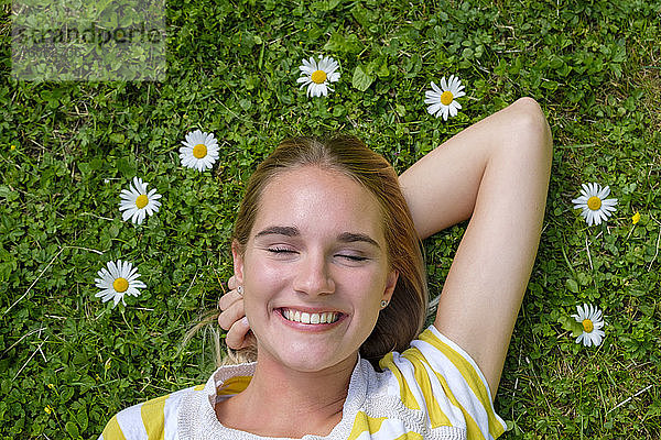Nahaufnahme einer lächelnden Frau mit geschlossenen Augen  die auf einer Wiese im Park liegt