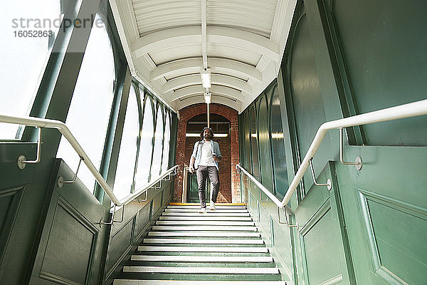 Junger trendiger Mann  der die Treppe am Bahnhof hinuntergeht