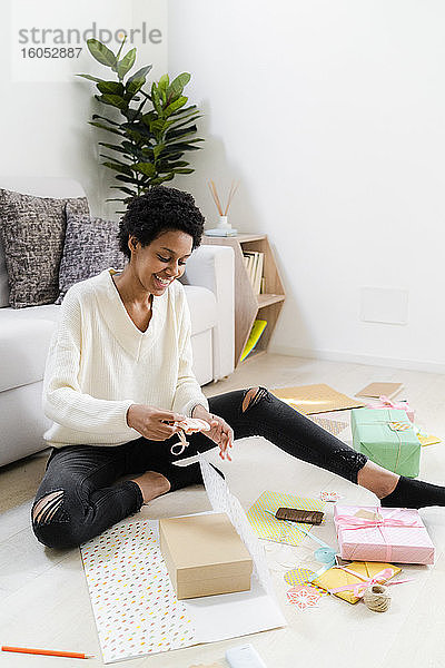 Lächelnde junge Frau  die zu Hause auf dem Boden sitzt und Geschenke einpackt